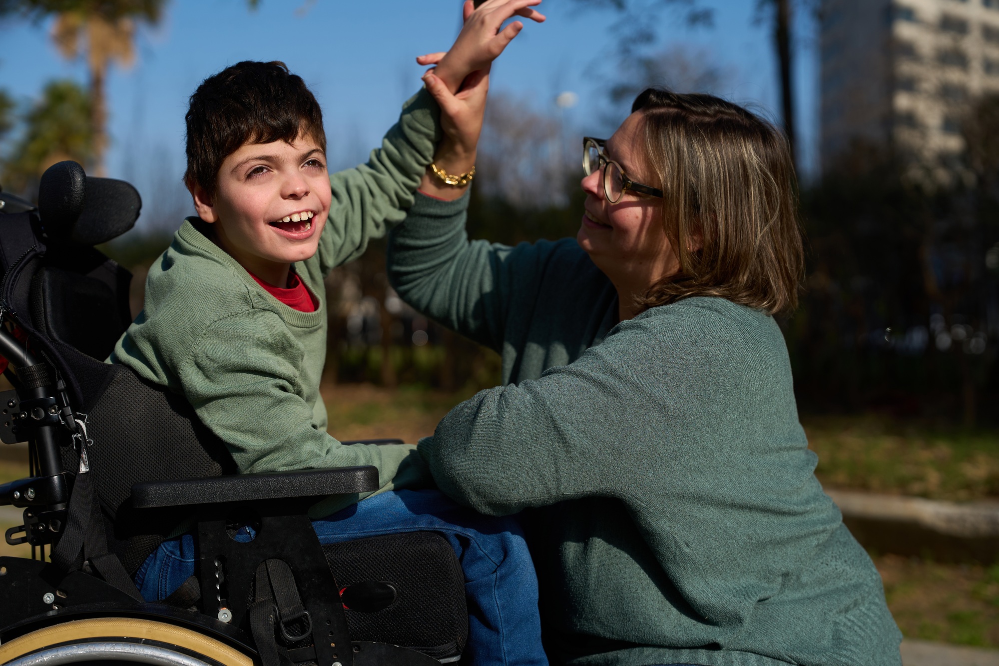 Happy child with disabilities giving high five to his educator in a park