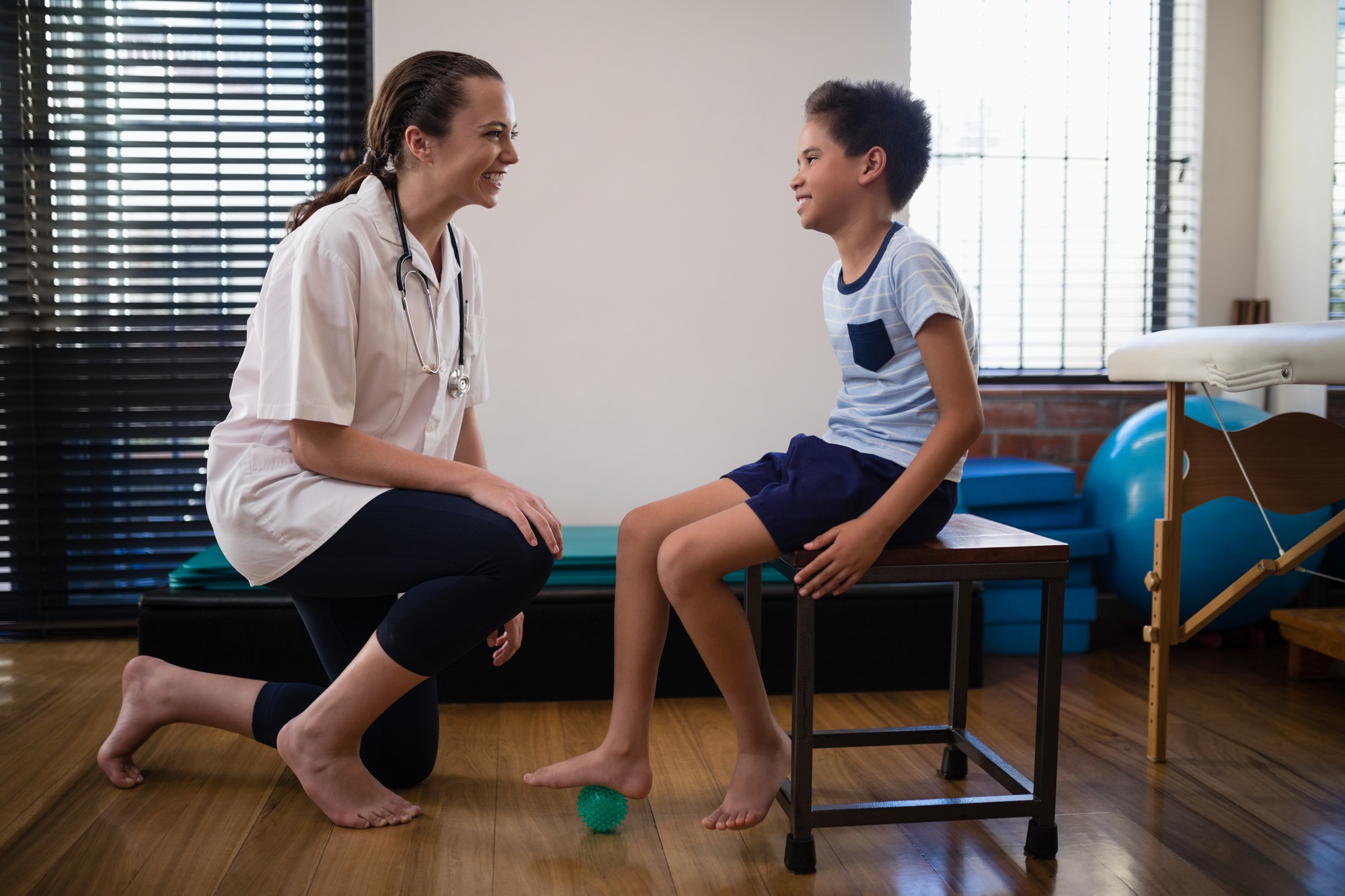 Smiling female therapist kneeling by boy stepping on stress ball